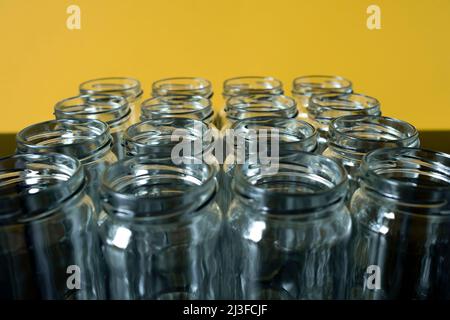 Frontale Aufnahme leerer Glasgefäße in einer Reihe auf einem gelb gefärbten Hintergrund. Ausgewählte Fokus oben auf dem Glas vor. Stockfoto