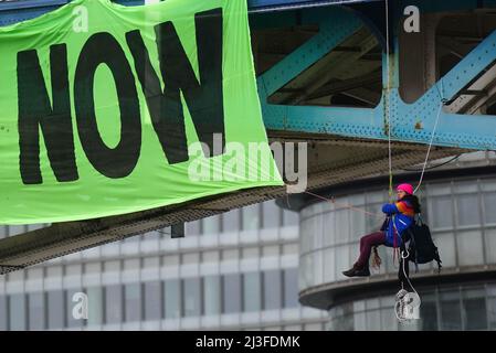 Aktivisten der Extinction Rebellion hängen an Hängeschlaufen neben einem riesigen Banner mit der Aufschrift „End fossile Fuels now“, während sie auf der Tower Bridge im Osten Londons, die für den Verkehr gesperrt wurde, protestieren. Bilddatum: Freitag, 8. April 2022. Stockfoto