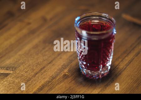 Auf einem Holztisch steht eine rote Tinktur aus Kristallglas Stockfoto