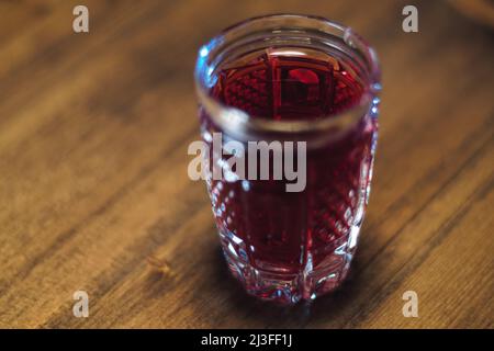 Auf einem Holztisch steht eine rote Tinktur aus Kristallglas Stockfoto