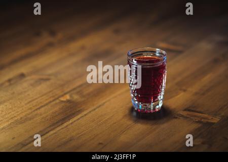 Auf einem Holztisch steht eine rote Tinktur aus Kristallglas Stockfoto