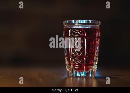 Auf einem Holztisch steht eine rote Tinktur aus Kristallglas Stockfoto