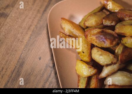 Gebackene knusprige Kartoffeln auf einem braunen Teller auf einem Holztisch Stockfoto