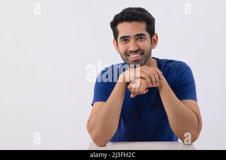 Studioaufnahme eines glücklichen jungen Mannes, der die Kamera ansah und dabei die Hände unter dem Kinn hielt Stockfoto