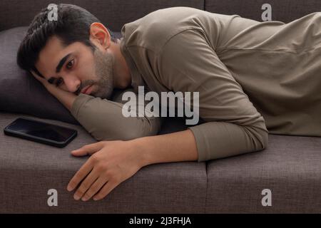 Porträt eines jungen Mannes, der auf dem Sofa liegt und ein Smartphone daneben hält Stockfoto