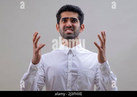 Porträt eines wütenden jungen Mannes in weißem Hemd, der die Kamera anschaut, wobei die Zähne zusammenknallen Stockfoto