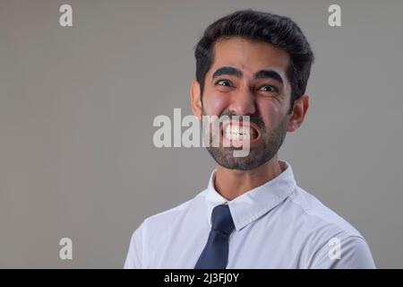 Porträt eines wütenden jungen Mannes in weißem Hemd, der die Kamera anschaut, wobei die Zähne zusammenknallen Stockfoto