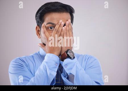 Porträt eines besorgten Geschäftsmannes, der das Gesicht mit den Händen bedeckt und die Kamera mit einem Auge anschaut Stockfoto