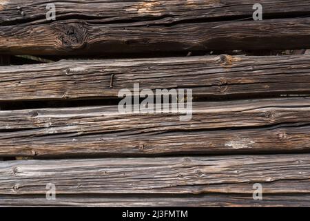 Nahaufnahme eines alten, verwitterten, sonnenverbrannten Stalls mit liegenden Baumstämmen als Wänden und gut sichtbarer Textur aus altem Holz als Hintergrund Stockfoto