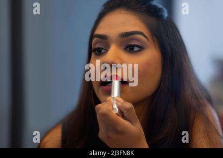 Nahaufnahme eines Porträts einer jungen Frau, die einen roten Lippenstift anwendet Stockfoto