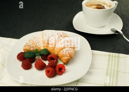 Appetitliche knusprige Croissants und frische Himbeeren auf einem weißen Teller. Französisches Frühstück. Frisch duftendes Gebäck und Himbeeren. Hintergrund und SPA kopieren Stockfoto