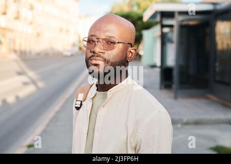 Porträt eines ernsthaften jungen schwarzen Mannes in Sonnenbrille, der am Busbahnhof steht und morgens auf den Transport wartet Stockfoto