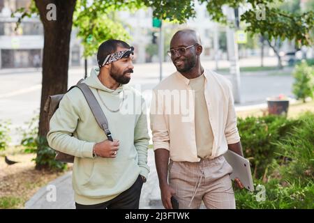 Positive junge multirassische Freunde, die nach dem Universitätsunterricht auf der Straße spazieren und sich unterhalten Stockfoto