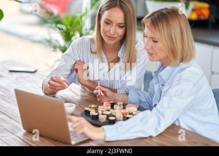 Nette zwei Erwachsene Mädchen im Haus, die Sushi essen und arbeiten Stockfoto