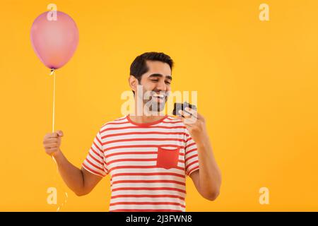 Porträt eines glücklichen jungen Mannes, der den Ballon in der Hand hält und ein Stück Kuchen isst Stockfoto