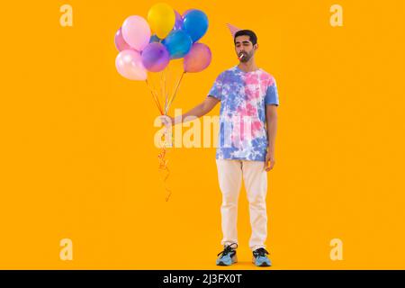 Trauriger junger Mann, der Ballons in der Hand hält und Party-Horn bläst Stockfoto