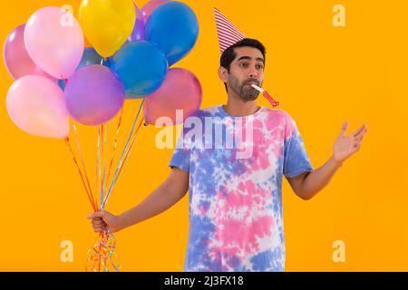 Junger Mann hält Ballons in der Hand und bläst Partyhorn Stockfoto