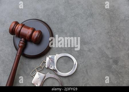 Thema „Recht“. Gerichtsverfahren in Sitzung. Richter Gavel Handschellen auf grauen Tisch in Anwaltsbüro oder Gerichtsverhandlung. Mallet von Richter auf Beton Stein grauen Hintergrund. Gerechtigkeit Menschenrechte Konzept Stockfoto