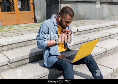 Junge konzentriert stilvolle afroamerikanische freiberufliche Geschäftsmann männlich arbeiten mit Laptop und Handy im Freien, auf der Treppe i sitzen Stockfoto