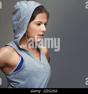 Sich der Fitness verschrieben. Aufnahme einer sportlichen jungen Frau, die einen Hoodie trägt und vor grauem Hintergrund posiert. Stockfoto