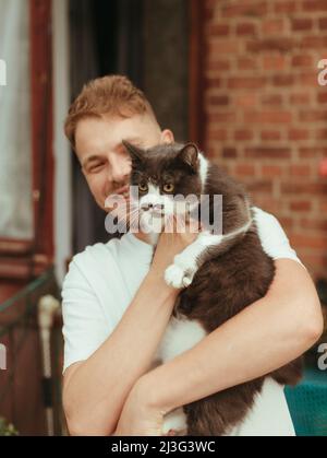 Mann, der die Katze in den Händen hält. British Grey Cat. Mann mit Katze lächelnd. Regen-Effekt Stockfoto