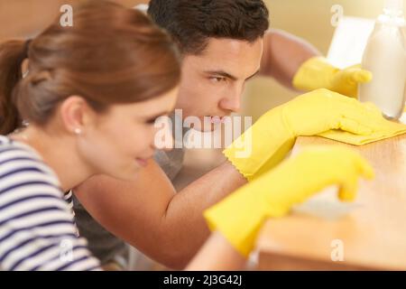 Sie perfektionierten die Reinigung zu einer Kunst. Aufnahme eines glücklichen jungen Paares, das gemeinsam ihre Küche putzte. Stockfoto