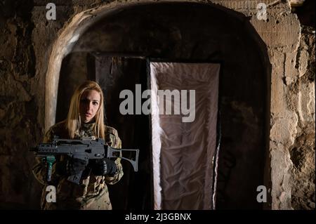 Kaukasische Frau in Armeeuniform, die ein Maschinengewehr hält und in der Nähe eines offenen Sarges steht. Stockfoto