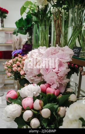 Blumenladen mit Blumen in transparenten Vasen: Pfingstrosen, Rosen, Hortensien - Schaufenster auf dem floristischen Markt. Stockfoto