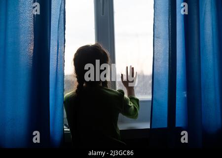 Junges Mädchen am Fenster, die Hände gegen das Fenster gedrückt, nachdenklich oder wollen heraus Stockfoto