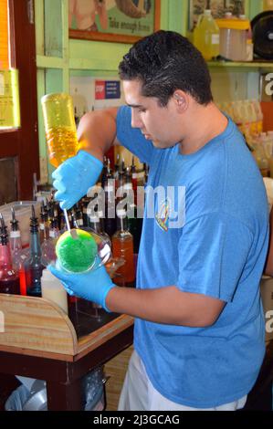Ein junger erwachsener Arbeiter fügt Shave Ice in einem Laden und Café auf Hawaii Aromen hinzu Stockfoto