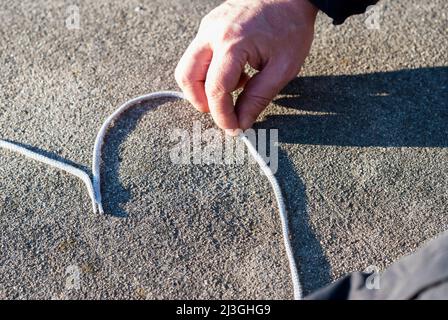 Hand macht ein Herz mit einer Schnur auf grauem Tisch mit Licht in horizontaler Stockfoto