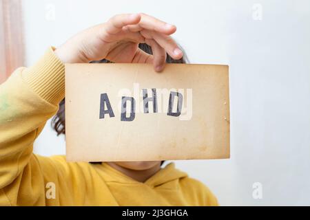 Hand des Kindes, das eine alte Papierseite mit der Abkürzung ADHD hält, die darauf geschrieben ist Stockfoto