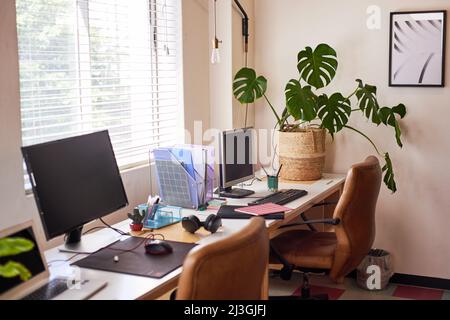 Eine Reihe leerer Schreibtische im Büro mit abgeschalteten Computern Stockfoto