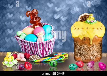 Osterfarbene Eier und Süßigkeiten im Korb. Süßigkeiten in Form eines Hasen.Bunte Ostern Set mit Eiern, Kuchen und Süßigkeiten auf einem defokussed Hintergrund w Stockfoto