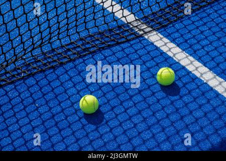 Zwei Paddle-Tennisbälle im Schatten des Netzes eines blauen Paddle-Tennisplatzes, Schlägersportkonzept Stockfoto