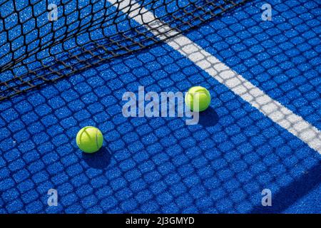 Zwei Paddle-Tennisbälle im Schatten des Netzes eines blauen Paddle-Tennisplatzes, Schlägersportkonzept Stockfoto