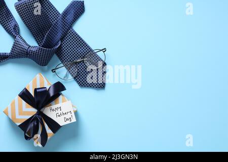 Happy Fathers Day Hintergrund. Flach legen Happy Fathers Day Geschenkbox, Krawatte, Gläser auf pastellblauem Tisch. Stockfoto