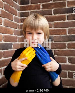 Kinder gegen Krieg. Weibliche Hände, in gelb und blau gemalt, umarmen und schützen ein Kind, ein Sohn. Konzept des Glaubens und der Hoffnung, Hilfe. Einheit, Unterstützung, c Stockfoto