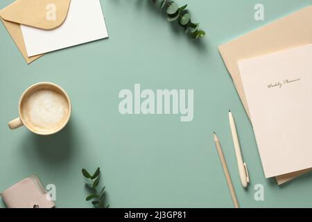 Eleganter femininer Arbeitsplatz mit einer Tasse Kaffee, Notizbüchern, Eukalyptusblättern auf dem grünen Tisch. Flach liegend, Draufsicht. Stockfoto