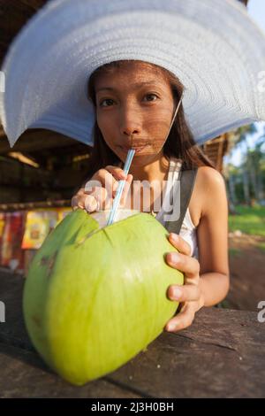 Philippinen, Palawan, Sabang Beach, eine junge philippinische Frau trinkt aus einer riesigen grünen Kokosnuss mit einem Stroh Stockfoto