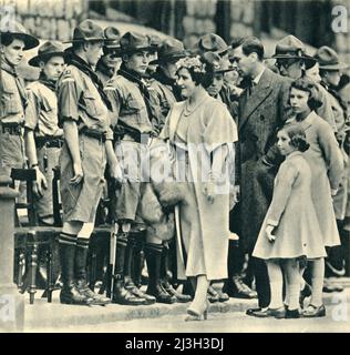 „Ihre Majestäten, der König und die Königin, mit den Prinzessinnen, die Jungen inspizieren, die trotz körperlicher Behinderungen zu Pfadfindern geworden sind“, 1944. König George VI, Elizabeth Queen Consort, Prinzessinnen Elizabeth (später Königin Elizabeth II) und Margaret mit behinderten Pfadfindern. Aus „Boy Scouts“, von E. E. Reynolds. [Collins, London, 1944] Stockfoto