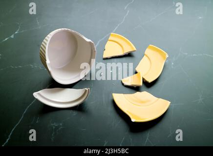 Zerbrochene weiße und gelbe Keramik, verstreut auf schwarzem Küchenboden Stockfoto
