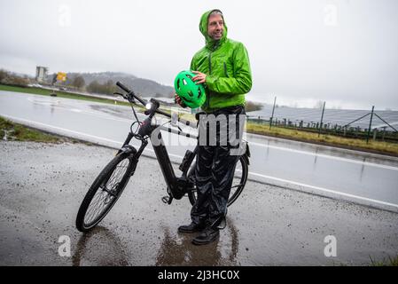 08. April 2022, Baden-Württemberg, Tübingen: Boris Palmer (Bündnis 90/die Grünen), Oberbürgermeister von Tübingen, erreicht bei starkem Regen einen Pressetermin mit Ministerpräsident Kretschmann auf seinem Fahrrad. Palmer zeigte dem Ministerpräsidenten den Solarpark 'Lustnauer Ohren' und informierte ihn über den aktuellen Stand des Projekts. Foto: Christoph Schmidt/dpa Stockfoto