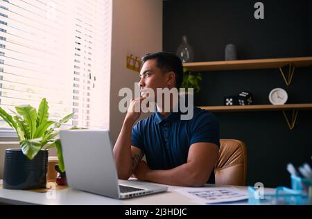 Ein junger Geschäftsmann sitzt und blickt aus dem Fenster und denkt an seinen Schreibtisch Stockfoto