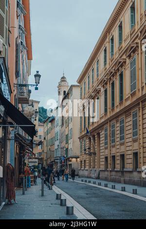Nizza, Frankreich - 10. März 2022: Menschen, die an Cafés und Geschäften in der Altstadt von Nizza vorbeilaufen, einem berühmten Touristenziel an der französischen Riviera. Stockfoto