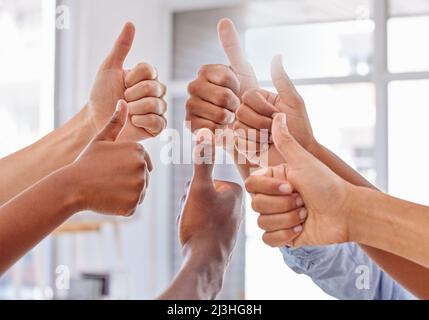 Daumen hoch für Teamarbeit. Zugeschnittene Aufnahme einer Gruppe von nicht erkennbaren Personen, die in einem Büro den Daumen nach oben zeigen. Stockfoto