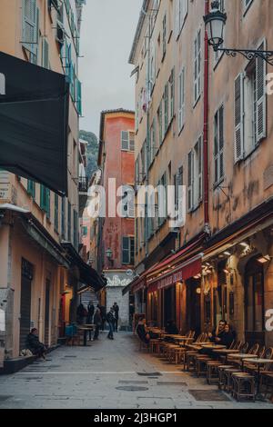 Nizza, Frankreich - 10. März 2022: Bars und Restaurants in einer schmalen Straße in der Altstadt von Nizza, einem berühmten Touristenziel an der französischen Riviera, pe Stockfoto