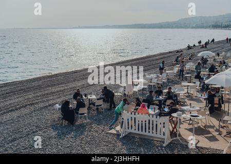 Nizza, Frankreich - 10. März 2022: Menschen sitzen und entspannen am Strandtisch eines Restaurants in Nizza, einem berühmten Touristenziel auf dem französischen Rivi Stockfoto