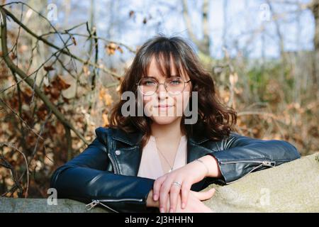 Selbstbewusste junge Frau auf einem Baumstamm im Wald Stockfoto