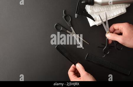 Friseurhände nehmen Friseurwerkzeuge auf dem schwarzen Tisch voller Accessoires auf. Draufsicht. Horizontale Zusammensetzung. Stockfoto